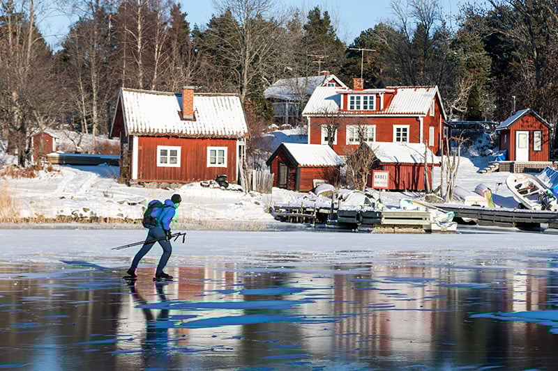 Man åker skridskor på is i svensk vintermiljö med röda hus i bakgrunden. Symboliserar smidigheten med automatisering av HR- och lönearbetet genom digitala flöden och AI.