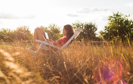 woman-sitting-on-a-deck-chair-on-a-meadow-using-di-2024-09-23-02-11-21-utc