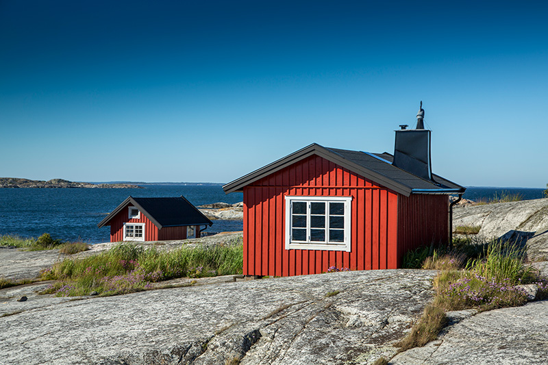 Rött hus i svensk skärgård, symboliserar stabil grund för HR-arbetet. Lär dig hur automatisering och digitala flöden frigör tid för strategiska HR-insatser i svenska kommuner.