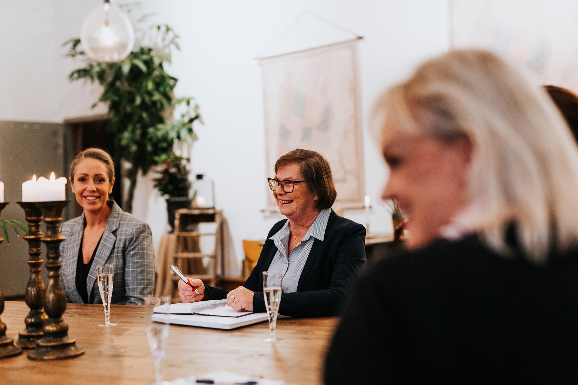 Äldre kvinna i glasögon och kollegor samarbetar runt ett bord. Bilden symboliserar trygghet i lönehanteringen genom teamarbete och en robust beredskapsplan (BCP).